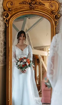 Bride holding a bouquet beside an ornate mirror, with her reflection visible.