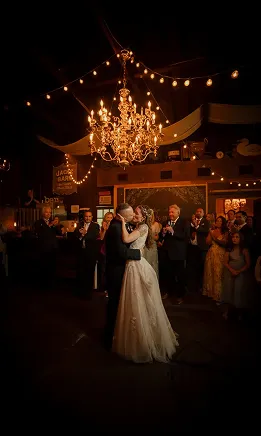Newlyweds dancing beneath a chandelier as wedding guests watch.