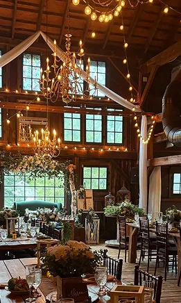 Chandeliers hanging from exposed wooden beams inside a rustic barn wedding venue.