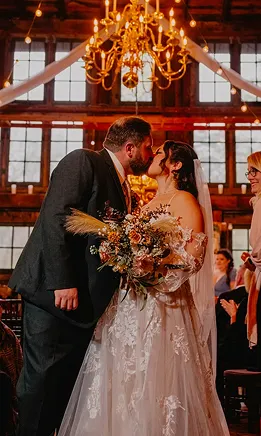 Newlyweds kissing beside a colorful floral arrangement inside the wedding venue.