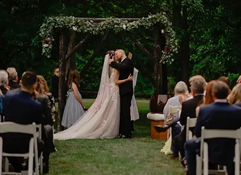 Couple exchanging vows beneath a garden arbor as guests look on.