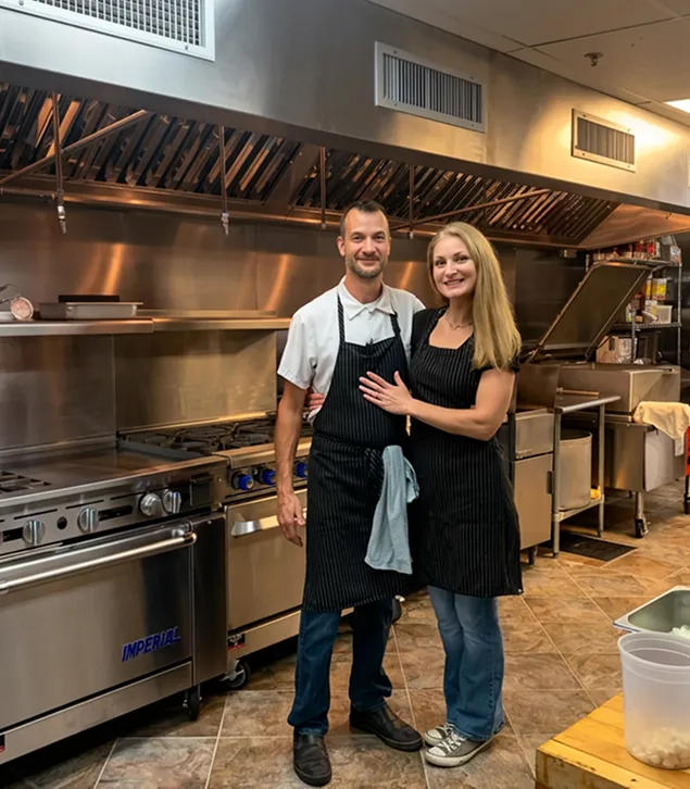 Two people posing together in a commercial kitchen.